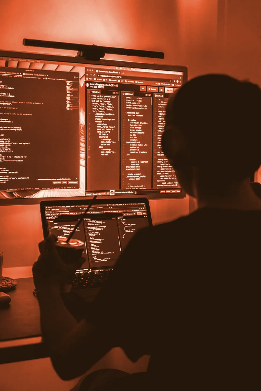 A developer hunched over glowing monitors late at night