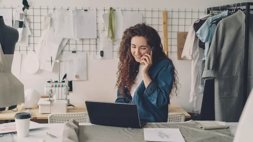 A small business owner on the phone while working on her laptop in her studio